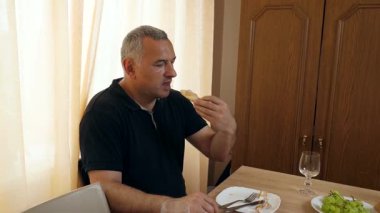 Bir adam evde masada otururken yemek yer..