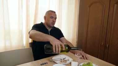 Bir adam evde bir masada otururken şarap içer..