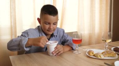 Çocuk masada otururken yoğurt yiyor.