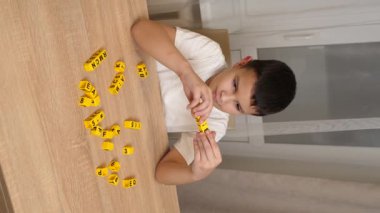 Bir çocuk masada otururken küplerden kelimeler üretiyor..