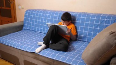 Bir çocuk kanepede otururken tahta üzerine bir kalemle resim çizer..