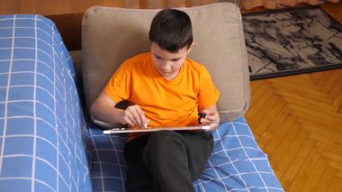 Bir çocuk kanepede otururken tahta üzerine bir kalemle resim çizer..