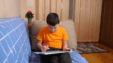 Bir çocuk kanepede otururken tahta üzerine bir kalemle resim çizer..