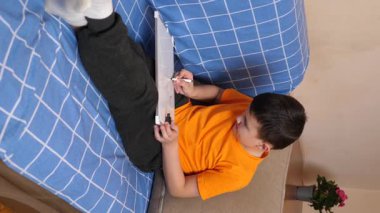 Bir çocuk kanepede otururken tahta üzerine bir kalemle resim çizer..