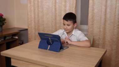 Bir çocuk masada otururken tablette oyunlar oynuyor..