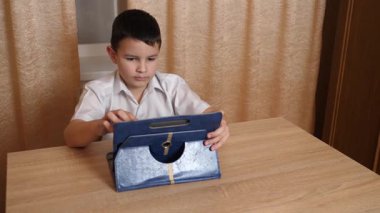 Bir çocuk masada otururken tablette oyunlar oynuyor..