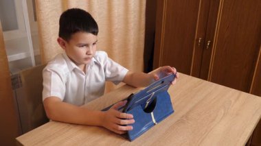 Bir çocuk masada otururken tablette oyunlar oynuyor..