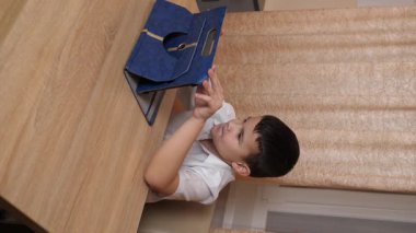 Bir çocuk masada otururken tablette oyunlar oynuyor..