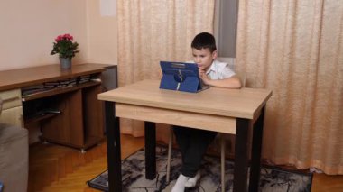 Bir çocuk masada otururken tablette oyunlar oynuyor..