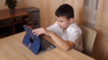 Bir çocuk masada otururken tablette oyunlar oynuyor..