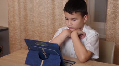 Bir çocuk masada otururken tablette oyunlar oynuyor..