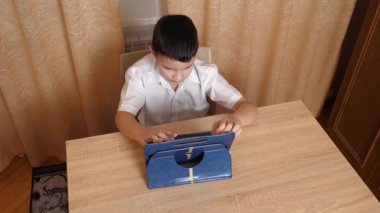 Bir çocuk masada otururken tablette oyunlar oynuyor..