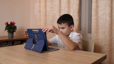 Bir çocuk masada otururken tablette oyunlar oynuyor..