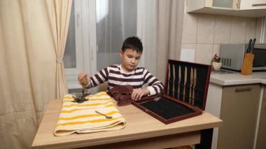 Oğlan çatal ve mutfak bıçaklarını siliyor. Ev işleri..