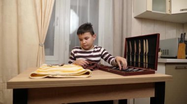 Oğlan çatal ve mutfak bıçaklarını siliyor. Ev işleri..