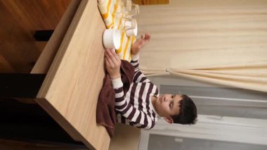 Oğlan bardakları ve bardakları havluyla siler. Ev işleri..