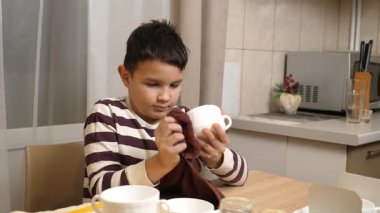 Oğlan bardakları ve bardakları havluyla siler. Ev işleri..