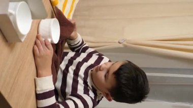 Oğlan bardakları ve bardakları havluyla siler. Ev işleri..