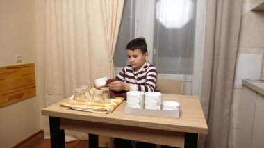 Oğlan bardakları ve bardakları havluyla siler. Ev işleri..