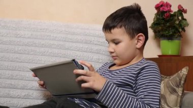 Bir çocuk kanepede otururken tablette oyun oynuyor..