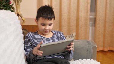 Bir çocuk kanepede otururken tablette oyun oynuyor..