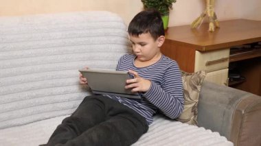 Bir çocuk kanepede otururken tablette oyun oynuyor..