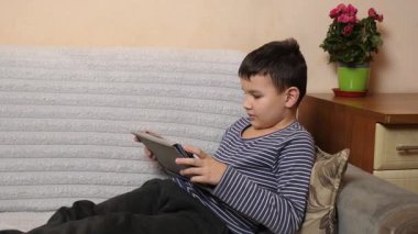 Bir çocuk kanepede otururken tablette oyun oynuyor..