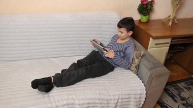 Bir çocuk kanepede otururken tablette oyun oynuyor..