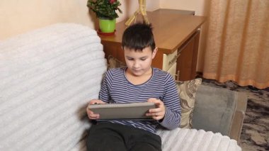Bir çocuk kanepede otururken tablette oyun oynuyor..