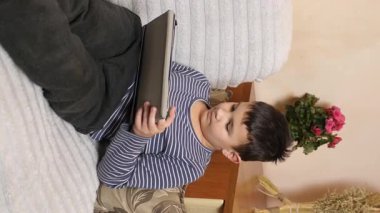 Bir çocuk kanepede otururken tablette oyun oynuyor..