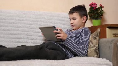 Bir çocuk kanepede otururken tablette oyun oynuyor..