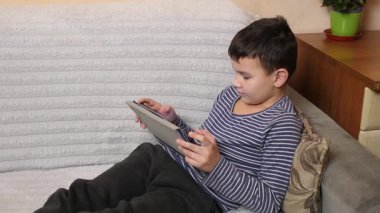 Bir çocuk kanepede otururken tablette oyun oynuyor..