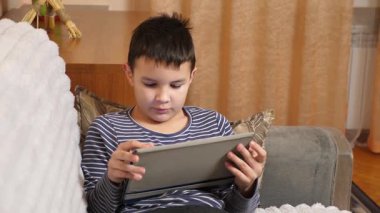 Bir çocuk kanepede otururken tablette oyun oynuyor..