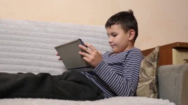 Bir çocuk kanepede otururken tablette oyun oynuyor..