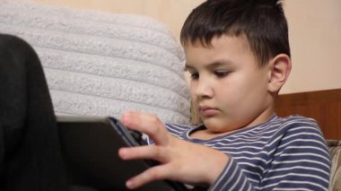 Bir çocuk kanepede otururken tablette oyun oynuyor..