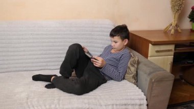 Bir çocuk kanepede otururken tablette oyun oynuyor..