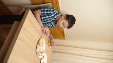 Bir çocuk masada otururken kurabiye yer ve çay içer..