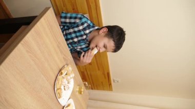 Bir çocuk masada otururken kurabiye yer ve çay içer..