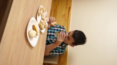 Bir çocuk masada otururken kurabiye yer ve çay içer..