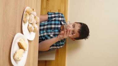 Bir çocuk masada otururken kurabiye yer ve çay içer..