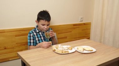 Bir çocuk masada otururken kurabiye yer ve çay içer..