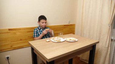 Bir çocuk masada otururken kurabiye yer ve çay içer..