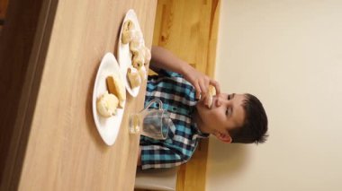 Bir çocuk masada otururken kurabiye yer ve çay içer..