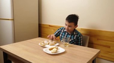 Bir çocuk masada otururken kurabiye yer ve çay içer..