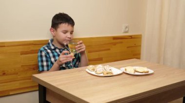 Bir çocuk masada otururken kurabiye yer ve çay içer..