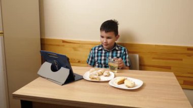 Bir çocuk masada otururken kurabiye yer ve çay içer..