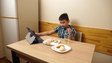 Bir çocuk masada otururken kurabiye yer ve çay içer..