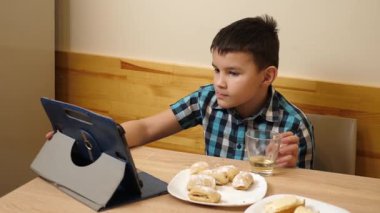 Bir çocuk masada otururken kurabiye yer ve çay içer..