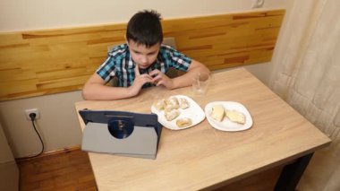 Bir çocuk masada otururken kurabiye yer ve çay içer..