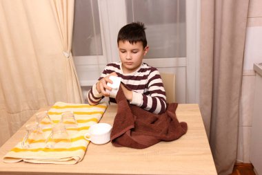 Oğlan bardakları ve bardakları havluyla siler. Ev işleri..